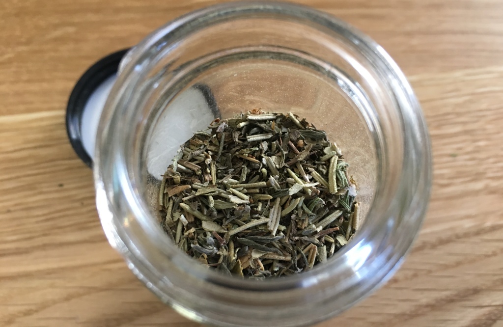 herbes de Provence in an open glass spice jar on a wooden counter